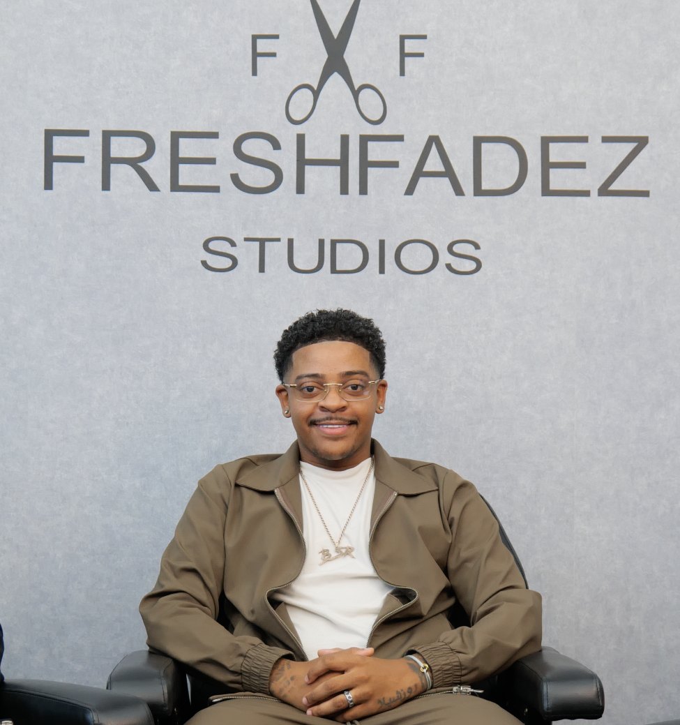 De oprichter van Fresh Fadez Studios, gezeten voor de logo-wand van de studio